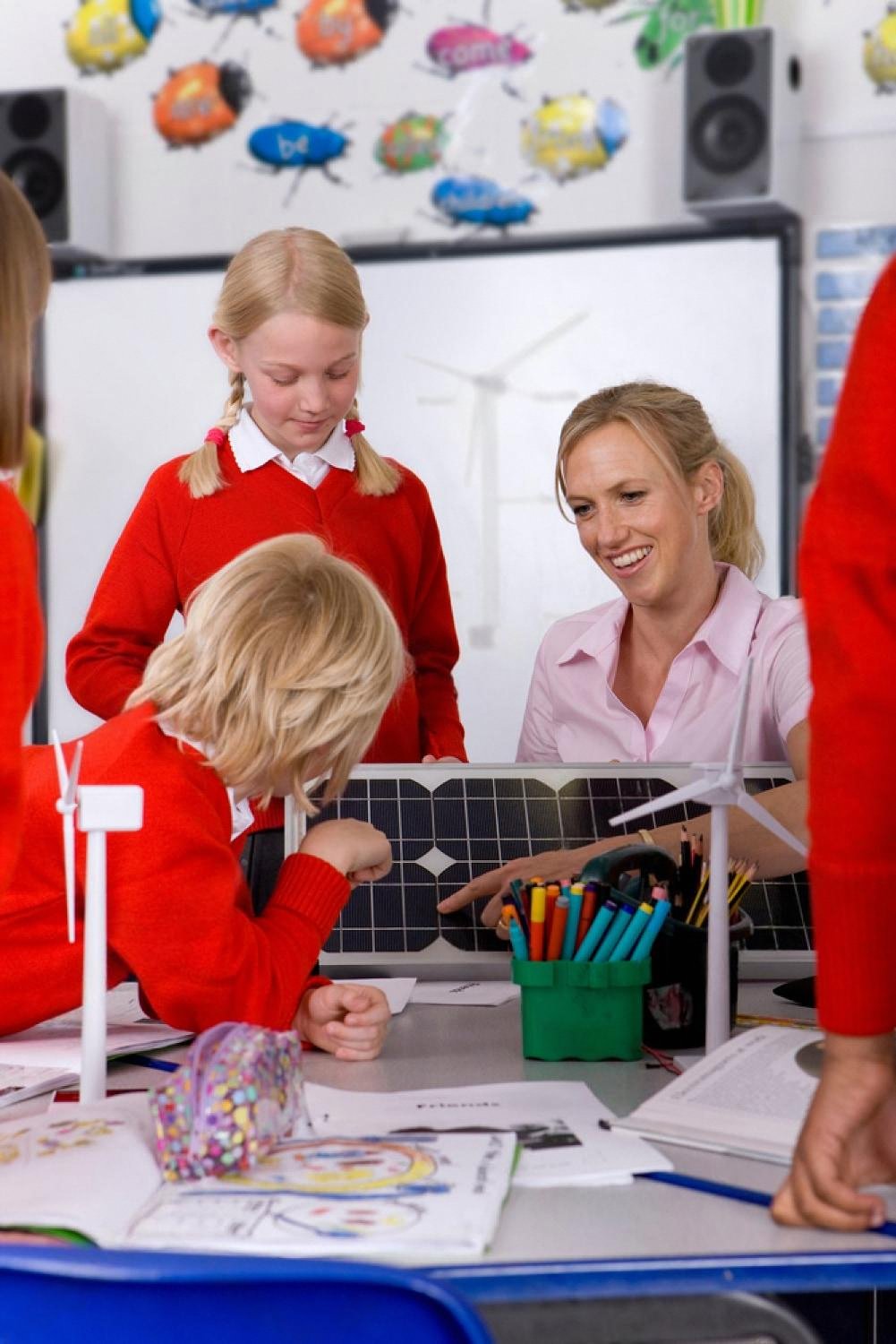 Elementary students and teacher working on a hands-on renewable energy project with solar panel and wind turbine models